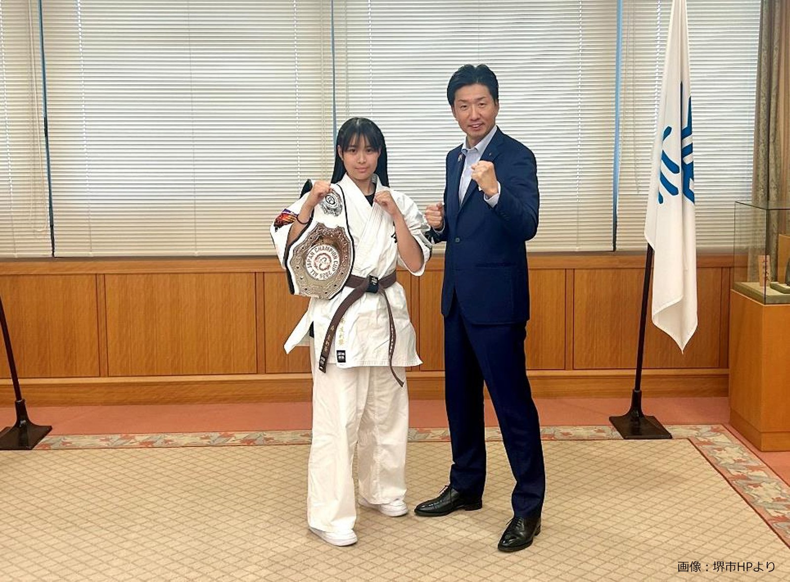 空手着姿の南友利葵選手が永藤英機市長と並び、盾を持って記念撮影する様子