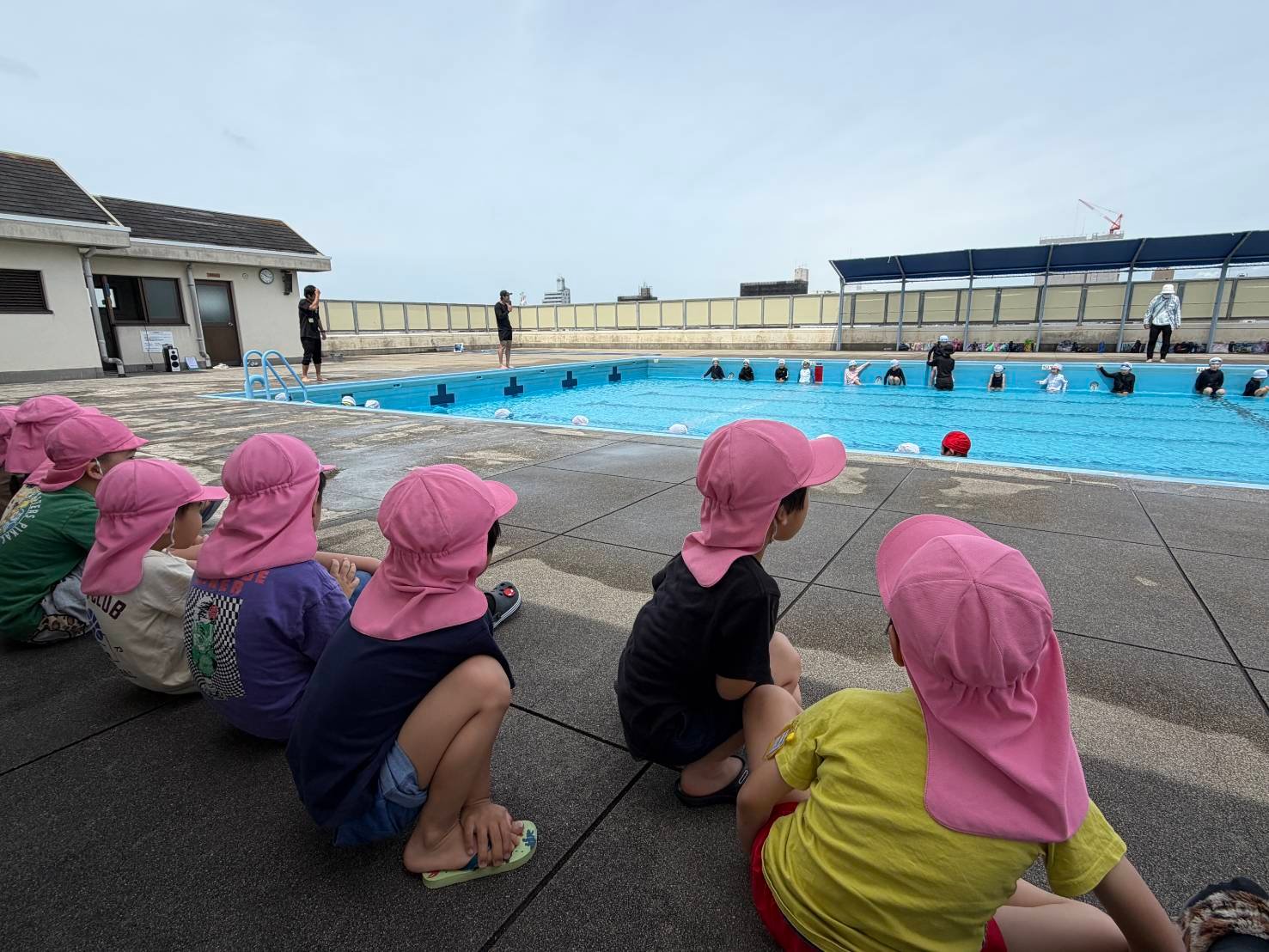 小学校のプールサイドで、園児たちが水泳授業の様子を見学している