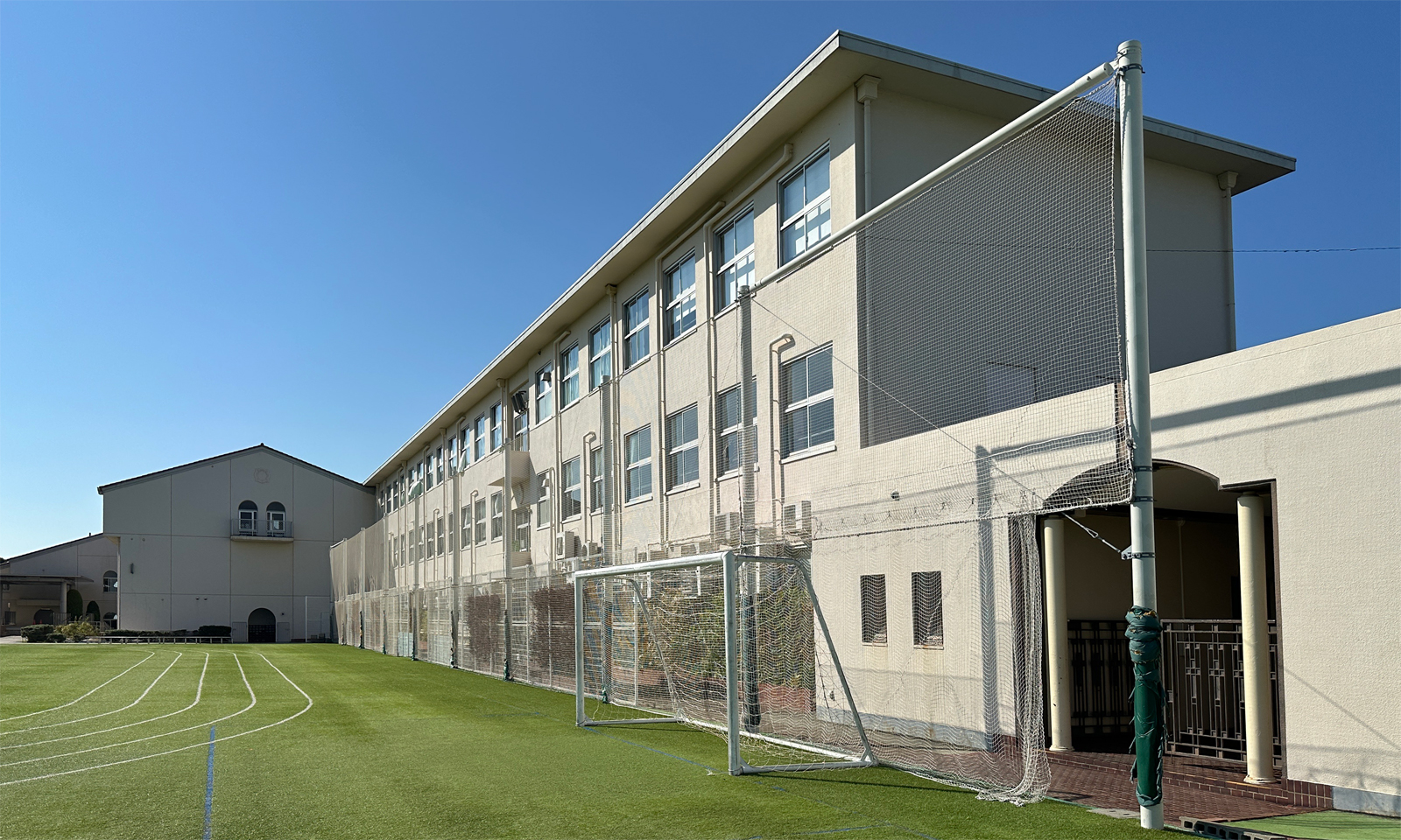 賢明学院小学校の校舎とグラウンド。人工芝のグラウンドにはトラックのラインやサッカーゴールが設置されている