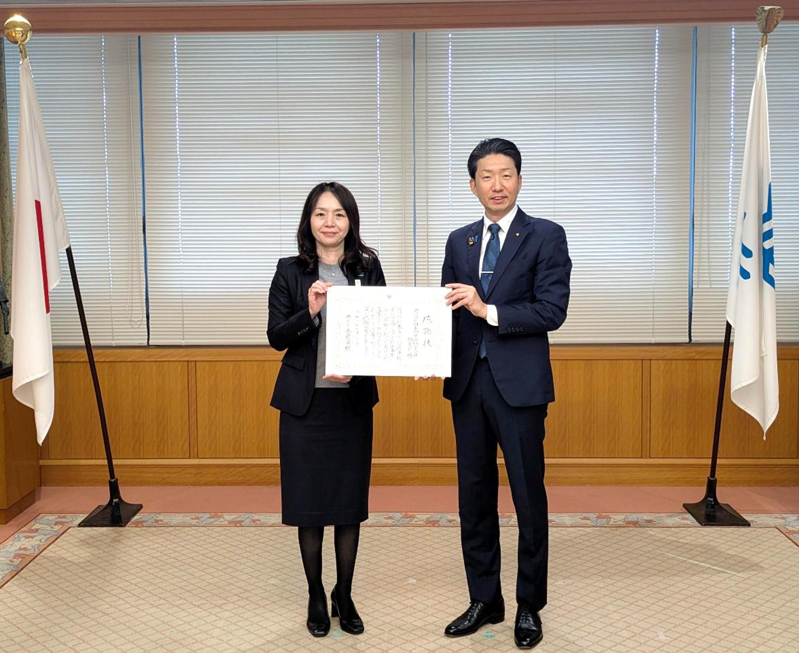 堺市役所で行われた感謝状贈呈式で、感謝状を持って並ぶ明治安田生命保険相互会社の新垣寿和子堺支社長（左）と永藤英機堺市長（右）
